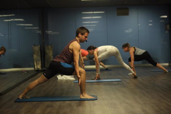 Archivo - Un entrenador imparte clase a varias personas en una clase de Body Balance en un gimnasio de Madrid.