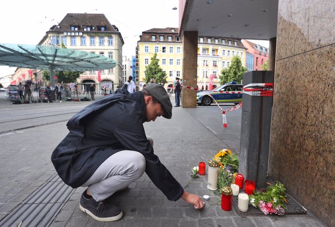 26 June 2021, Bavaria, Wuerzburg: A young man lights a candle in front of a closed and cordoned off shop in the city centre, where three people have been killed and five injured in a knife attack in downtown Wuerzburg on Friday. The alleged attacker was