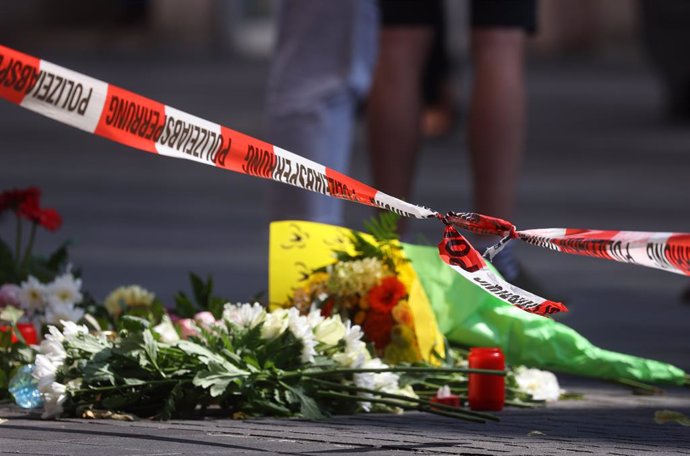 26 June 2021, Bavaria, Wuerzburg: Candles and flowers lie in front of a closed and cordoned off shop in downtown Wuerzburg, where three people have been killed and five injured in a knife attack on Friday. The alleged attacker was caught and detained, p