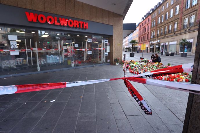 27 June 2021, Bavaria, Wuerzburg: Candles and flowers lie in front of a closed and cordoned off shop in downtown Wuerzburg, where three people have been killed and five injured in a knife attack on Friday. The alleged attacker was caught and detained, p