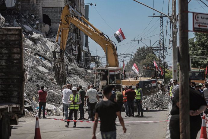 05 June 2021, Palestinian Territories, Gaza City: Palestinians watch an excavator run by an Egyptian team clearing up the rubble of Al-Shorouk Tower that was hit and destroyed during the recent Israeli airstrikes. The Egyptian government had sent excava