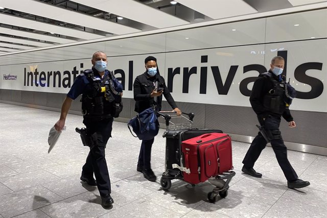 Archivo - 18 January 2021, United Kingdom, London: A passenger walks with police officers as he pushes a trolley through the arrival hall of Terminal 5 at London's Heathrow Airport, passengers arriving from anywhere outside the UK must have proof of a n