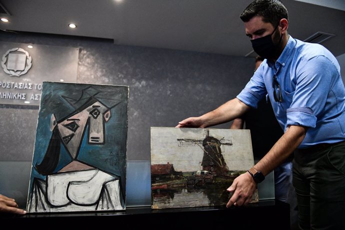 29 June 2021, Greece, Athens: A police officer holds Mill In The Evening (R), a recovered painting dated back to 1905 by Dutch painter Piet Mondrian, next to Woman's Head, a recovered painting dated back to 1939 by Spanish painter Pablo Picasso. Greek p
