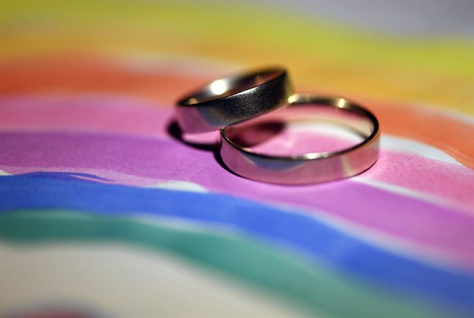 Archivo - FILED - 02 October 2017, Potsdam: A general view of two wedding rings placed on a painted rainbow-flag. Following the introduction of same-sex marriage in Germany, more than 70,000 same-sex couples in Germany had married or had their civil par