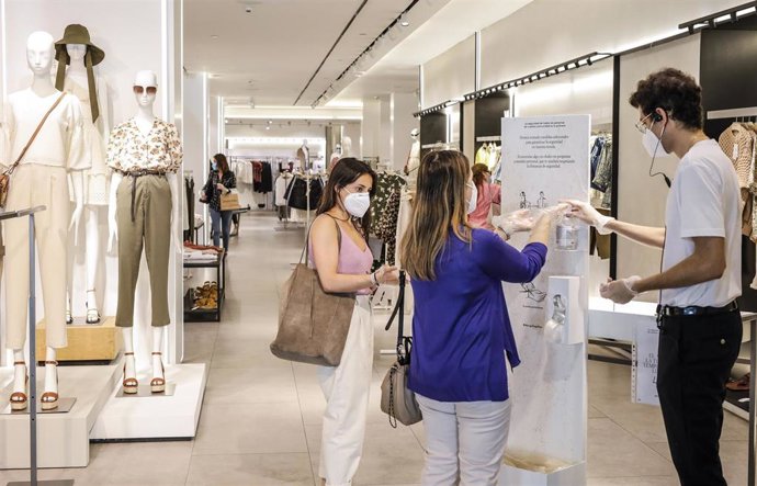 Archivo - Dos clientas se desinfectan las manos con gel hidroalcohólico a la entrada de una tienda de ropa