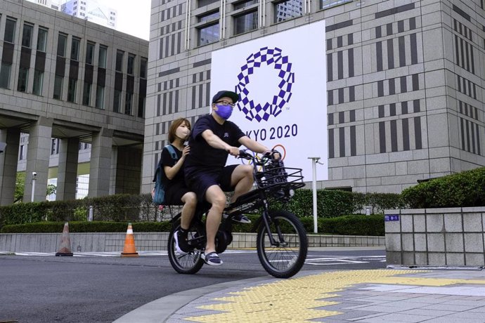 Una pareja pasea en bici por delante del cartel de los Juegos Olímpicos de Tokyo 2020.