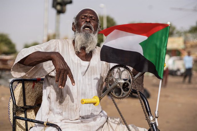 Archivo - 12 April 2019, Sudan, Khartoum: A Sudanese man holds the national flag as he sits on a wheel chair during a sit-in protest outside the Defence Ministry, to demand the formation of a civilian government, a day after the military took power and 