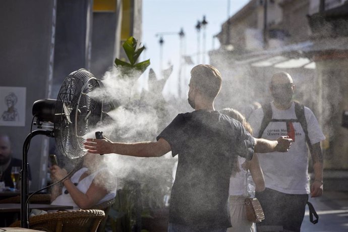 Un chico se refresca del calor con un difusor de vapor de agua de un restaurante de la calle Alcalá, en Madrid