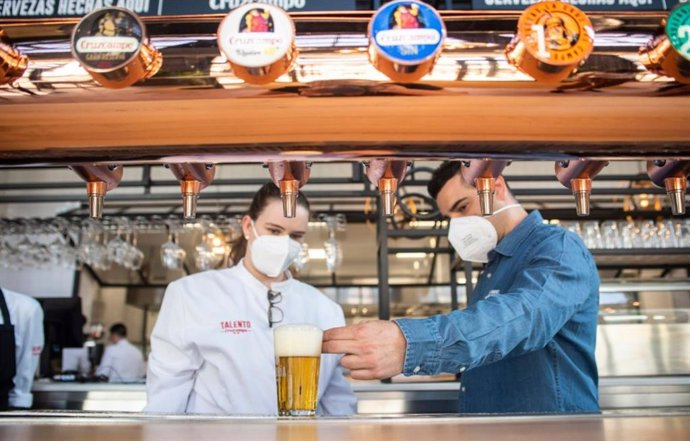 Dos camareros sirviendo una cerveza Cruzcampo en su establecimiento.