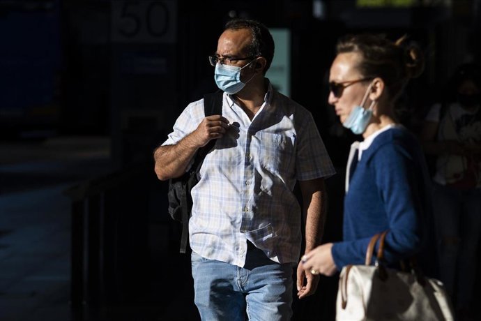 Un hombre y una mujer, con y sin mascarilla en una calle.