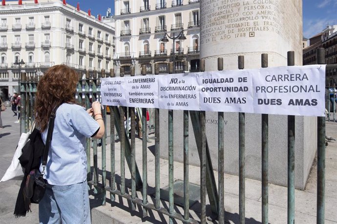 Archivo - Una mujer pega varios carteles con consignas durante una concentración en la Puerta del Sol con motivo del Día Internacional de la Enfermería.