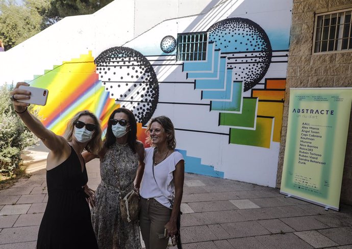 Tres mujeres se hacen una foto junto a uno de los murales que componen el proyecto 'Abstracte, un riu d'art', en las escaleras frente a la Rosaleda y el Palau de Les Arts
