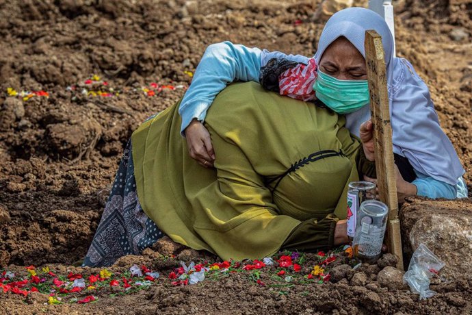 Dos mujeres lloran en la tumba de un ser querido que ha fallecido a causa de la COVID-19 en Yakarta Septentrional, Indonesia. 