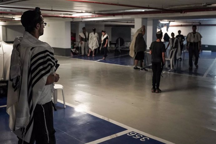 25 June 2021, Israel, Jerusalem: Jewish men, covered in prayer shawls, conduct their morning prayers in an underground parking lot while maintaining the social distancing. Israel reintroduced the mandatory wearing of face masks indoors on Friday in a bi