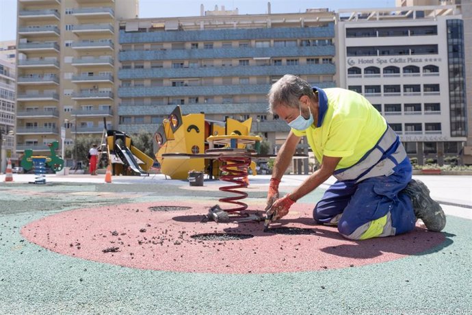 Operarios municipales reparan el suelo de caucho de un parque infantil