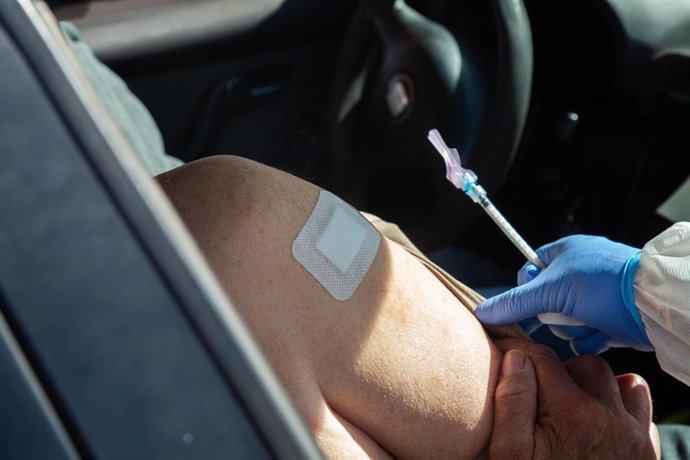 Archivo - Una sanitaria vacuna a una persona en un coche.