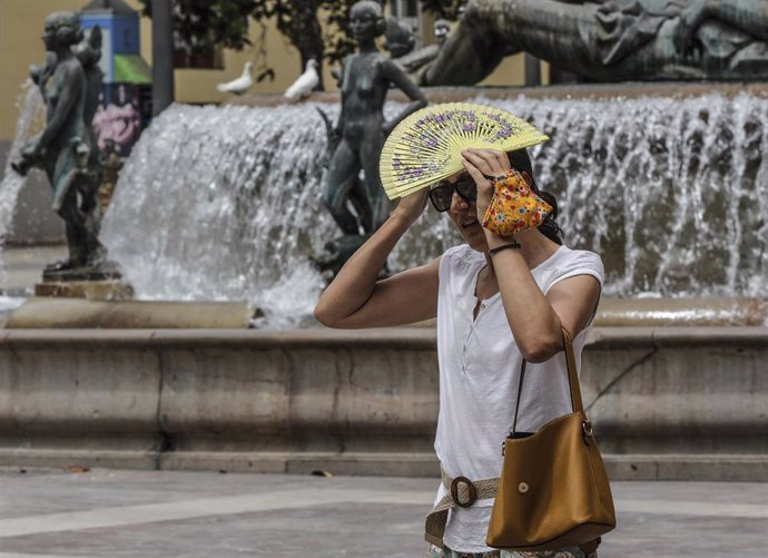 Una mujer se tapa la cabeza con un abanico para guarecerse de las altas temperaturas cerca de una céntrica fuente en Valncia