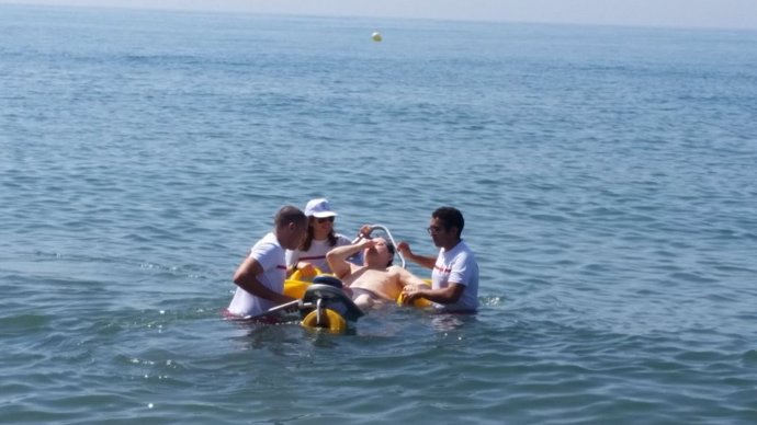 Efectivos de Cruz Roja ayudan a una persona con discapacidad en un baño en la playa dentro del programa de baños asistidos