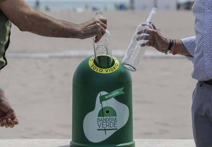 Dos personas tiran una botella de vidrio en uno de los contenedores que simbolizan el inicio de la campaña de verano Movimiento Banderas Verdes: campaña por una recuperación verde en la hostelería, en el Paseo Marítimo de Valncia. 