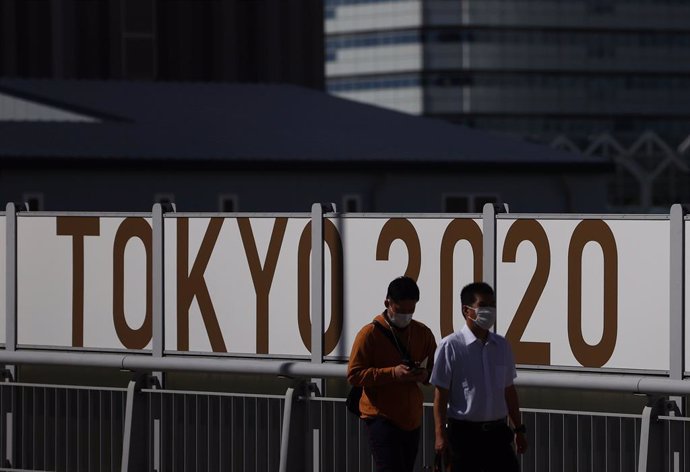 Japonenses utilitzen mascarillas durant la pandmia de COVID-19 amb un cartell dels Jocs Olímpics de Tquio a les seves esquenes