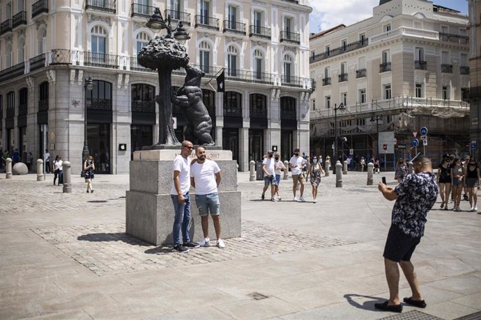 Un hombre toma una foto a otros dos, sin mascarilla en la Puerta del Sol,