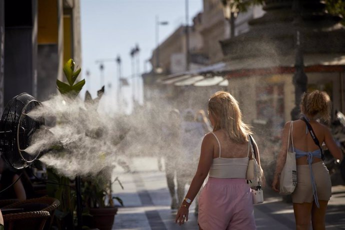 Varias personas caminan al lado de un difusor de vapor de agua, en una foto de archivo