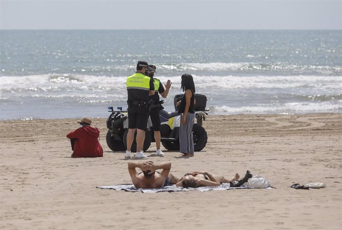 Archivo - Dos policías municipales hablan con una mujer en una playa de Valncia (archivo)