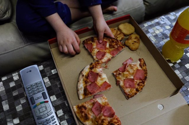 Archivo - Un niño come pizza del menú infantil de Telepizza mientras ve la televisión en su casa