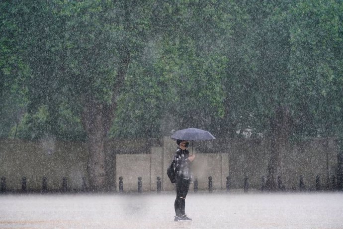 25 July 2021, United Kingdom, London: A woman uses an umbrella to protect herself from heavy rain in Horse Guards Parade, Westminster. Thunderstorms bringing lightning and torrential rain to the south are set to continue until Monday, forecasters have s
