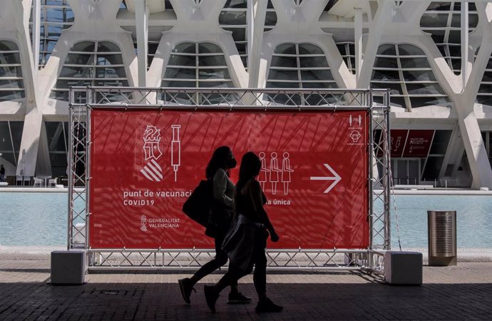 Archivo - Dos personas pasan por un cartel que indica el punto de vacunación de la Ciudad de las Artes y las Ciencias de Valncia. 