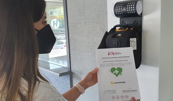 Hefame se certifica como 'Empresa cardioprotegida'. En la imagen, una empleada muestra el certificado ante un desfibrilador