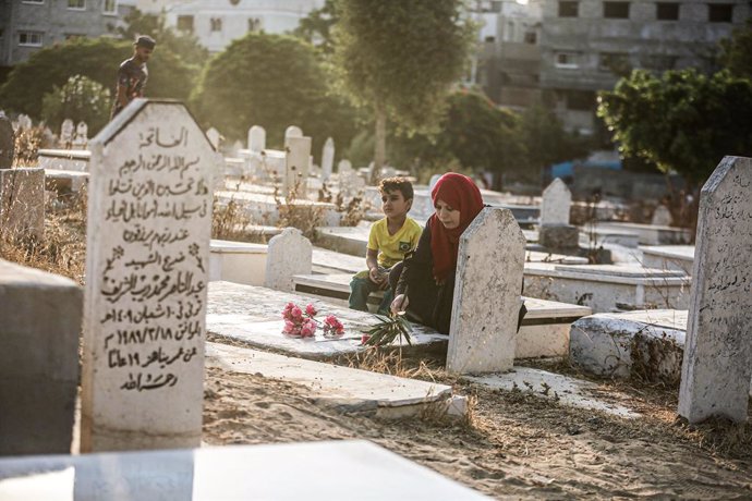 20 July 2021, Palestinian Territories, Gaza City: A Palestinian family visits the graves of their relatives during the Eid al-Adha at a cemetery in Gaza city. Eid al-Adha is the holiest feast in Islam, during which Muslims slaughter cattle and sheep to 