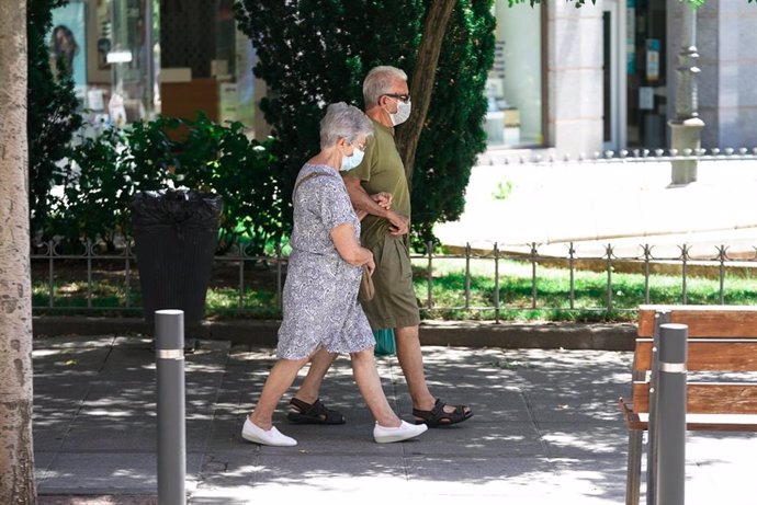 Una pareja de ancianos con mascarilla camina por la calle cogida del brazo.