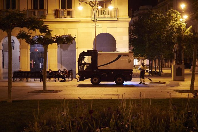 Archivo - Unos jovenes sentados mientras un trabajador de limpieza trabaja en la Plaza del Castillo alrededor de la media noche