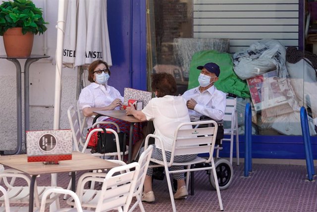 Ancianos con mascarilla conversan sentados en la terraza de un bar.