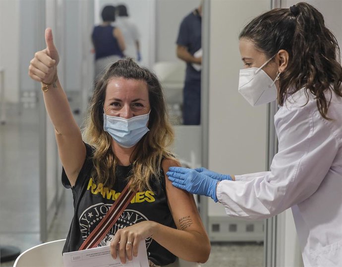 Una joven sonríe y saluda mientras recibe la vacuna contra el Covid-19 a una joven.