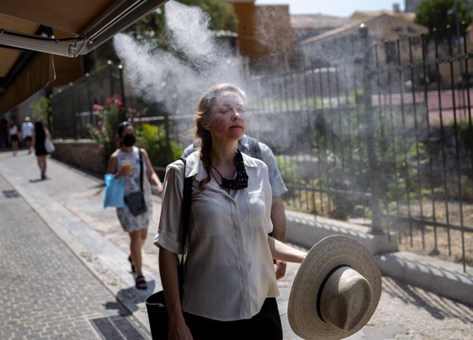 31 July 2021, Greece, Athens: A tourist walks through a mist of water sprayed outside a cafe amid temperatures that reached above 40 degrees. Photo: Angelos Tzortzinis/dpa