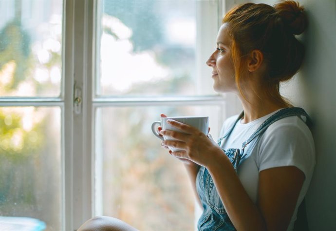 Mujer tomando una taza de café junto a la ventana,