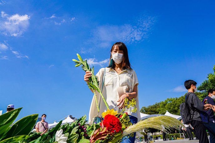 06 August 2021, Japan, Hiroshima: A woman wearing a face mask places flowers at Peace Memorial Park, as Hiroshima marks the 76th anniversary of the atomic bombing by the United States during World War II. Photo: Jinhee Lee/SOPA Images via ZUMA Press Wir