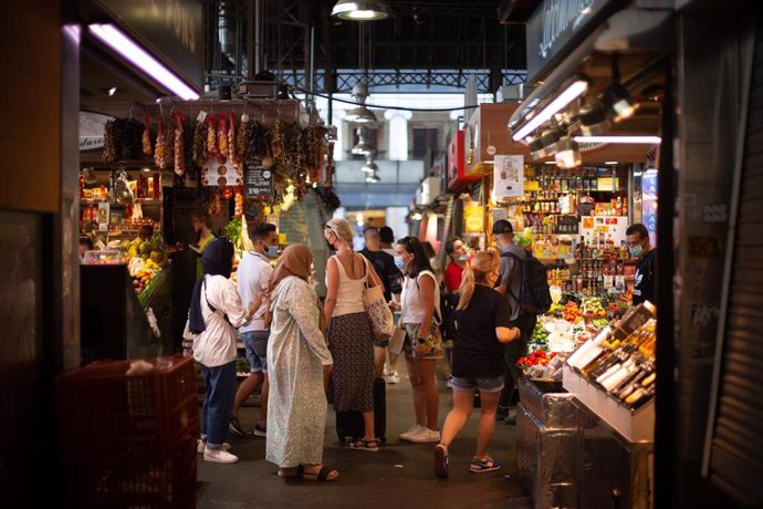 Varias personas observan puestos de venta de comida en el mercado de La Boquería, a 5 de agosto de 2021, en Barcelona, Cataluña, (España).