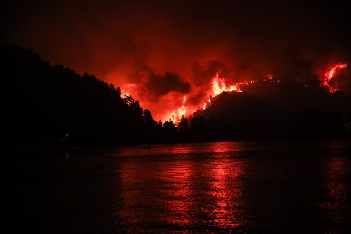 06 August 2021, Greece, Limni: Fire and smoke rise from burned ground in a wooded area in Limni village in the northwestern part of the island of Euboea, Greece. Since the early hours of the morning, strong westerly winds continued to fuel the numerous 