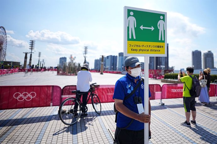 24 July 2021, Japan, Tokyo: A staff member holds a sign with a symbol and the words "Keep physical distance" to keep enough distance to protect themselves and others from contracting the coronavirus during the Tokyo 2020 Olympic Games. Photo: Michael Ka