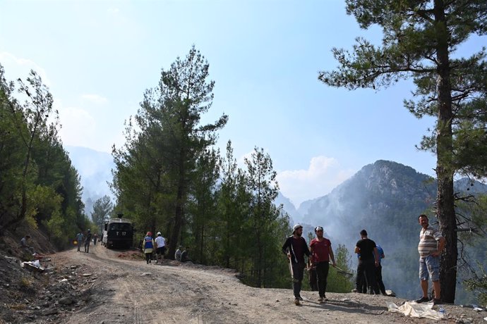 07 August 2021, Turkey, Koeycegiz: Helpers stand on a forest path while smoke rises in the background over the landscape of the community in the western Turkish town of Mugla. Ten days ago, fires broke out in numerous provinces across Turkey. Vast areas