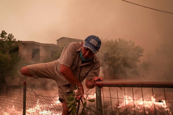 08 August 2021, Greece, Pefki: A man climbs over a fence to fuita the flames during a wildfire at Pefki village on Evia island, about 189 kilometers north of Athens. Photo: Pefki/Eurokinissi via ZUMA Press Wire/dpa