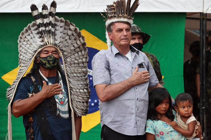 Archivo - HANDOUT - 27 May 2021, Brazil, Sao Gabriel da Cachoeira: Brazilian President Jair Bolsonaro (C)wears a traditional feather hat while attending the inauguration of the Rodrigo e Cibele wooden bridge with indigenous people in Sao Gabriel da Cac