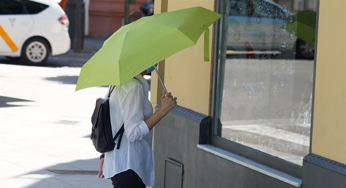 Archivo - Mujer pasea con un  paraguas amarillo por el puente de triana por el calor en foto de archivo.