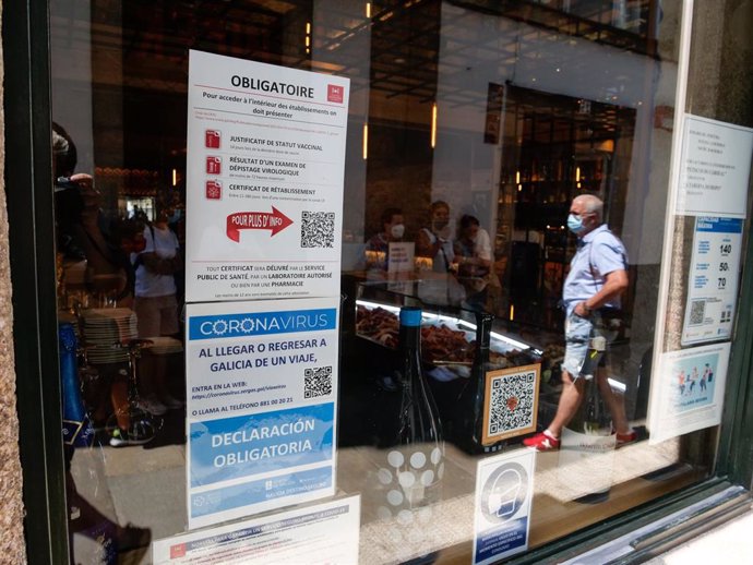 Carteles en diferentes idiomas de indicaciones de obligatoriedad de presentar certificados antes de acceder al interior, en una marisquería de la Rua do Franco, en Santiago.