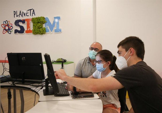 Dos jóvenes, participantes en el taller, explican su trabajo al consejero Cigudosa