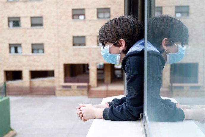 Archivo - Un niño con una mascarilla se asoma a la ventana de su casa 