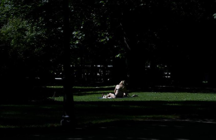 Archivo - Una joven toma el sol en el césped en el Parque del Retiro en Madrid.